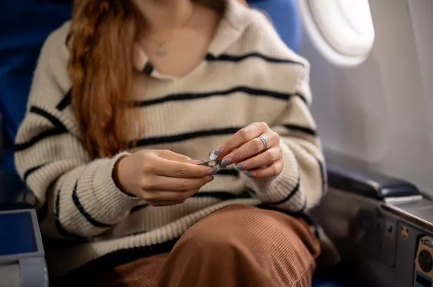 A close-up of a woman taking a pill at her seat on a flight 