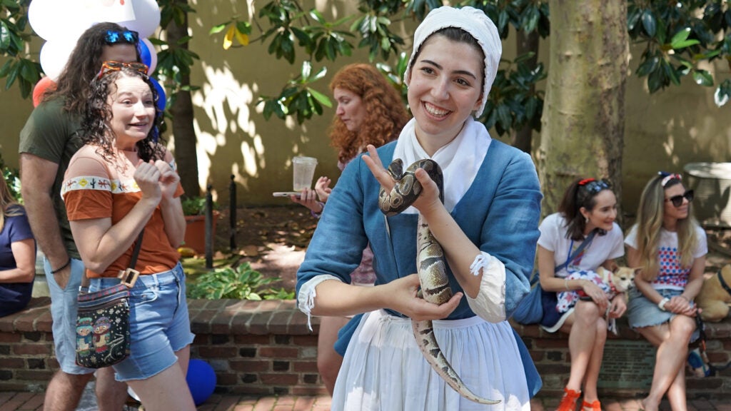 A woman dressed in 18th century garb holds a ball python