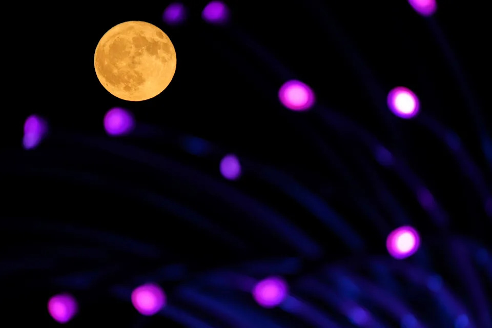 The buck moon rises above an art installation at a park in Leawood, Kan.
