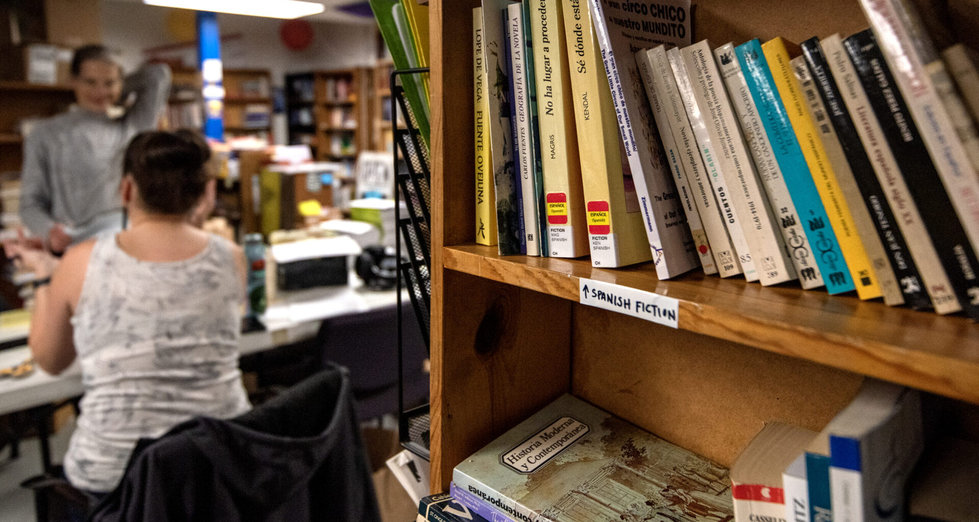 A bookshelf is stocked with books in a room where volunteers work.