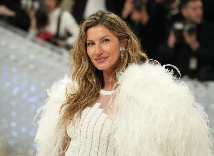 Person in elegant feathered gown posing on red carpet, surrounded by photographers