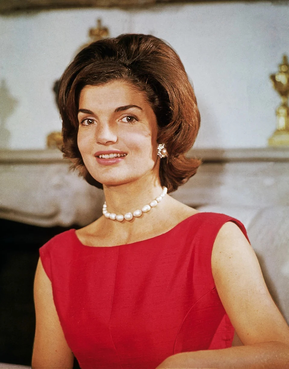 Jackie Kennedy wearing a sleeveless red dress with pearls.