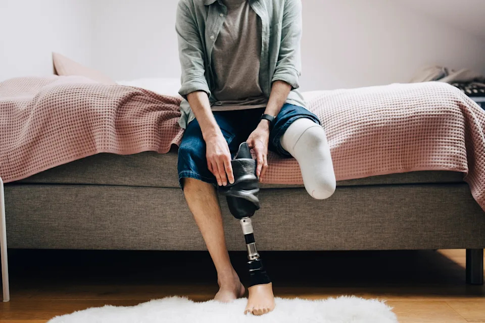 A person sitting on a bed is adjusting a prosthetic leg, creating an empowered and personal moment of daily life adaptability