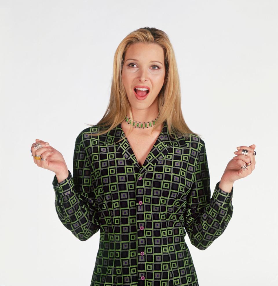 Person in a patterned outfit, open-mouthed with hands raised, stands in a playful pose