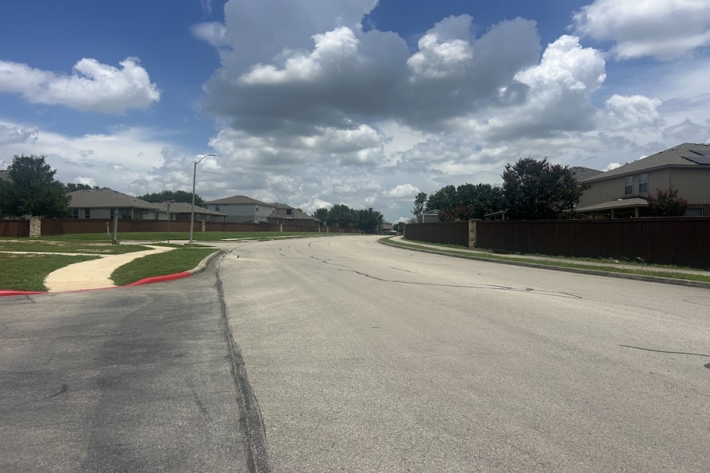 A residential street is shown on a partly cloudy afternoon in Cibolo, TX
