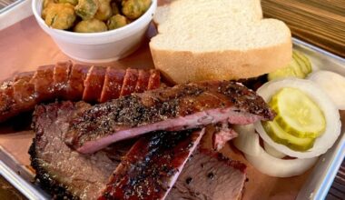 A plate of barbeque meats and bread with a side of pickles and okra