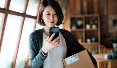 A person looking at a phone with a cardboard box in their hand.