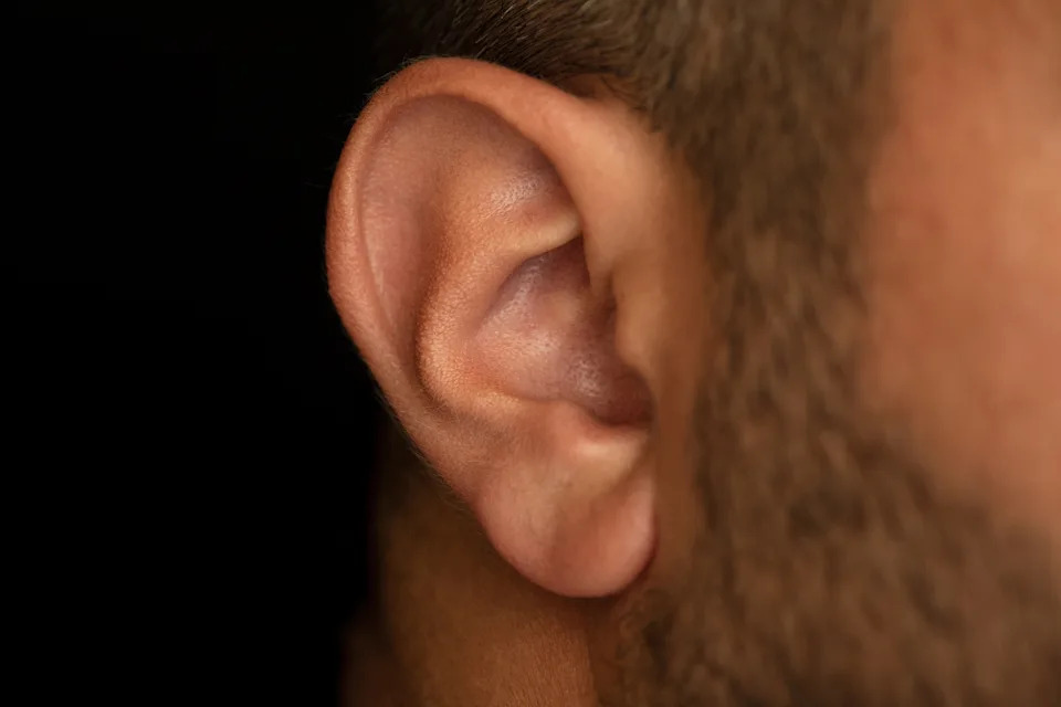 Close-up of a person's ear and part of their cheek against a dark background