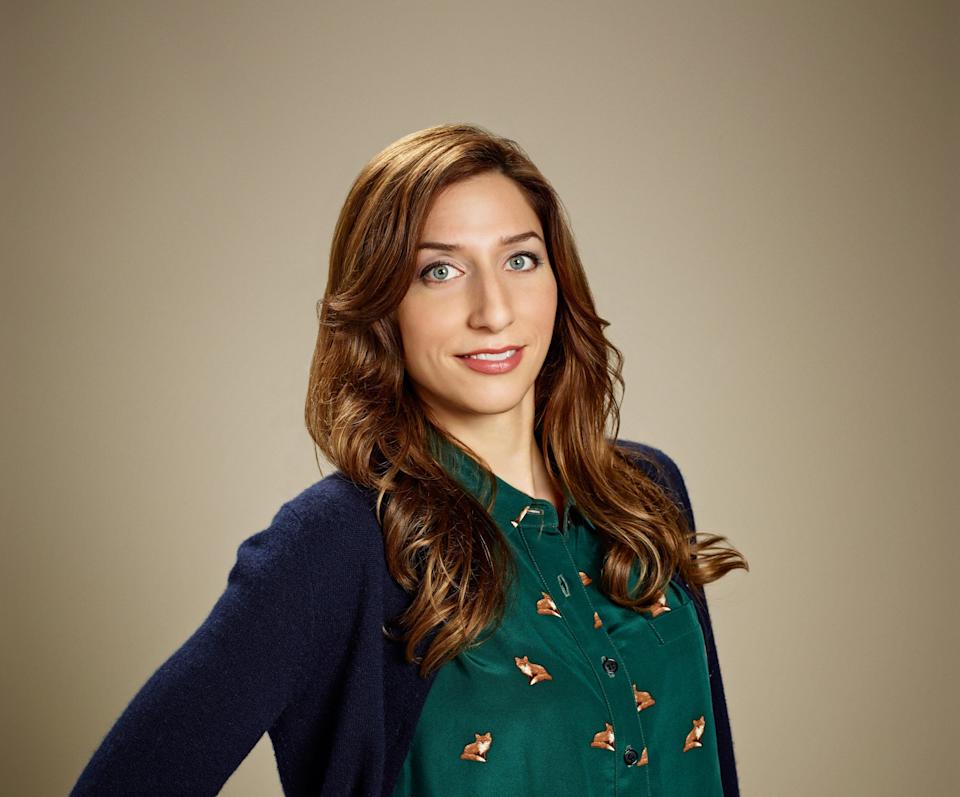 Person wearing a patterned dress with a cardigan, posing with one hand on hip