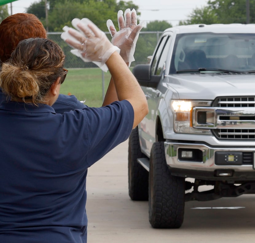 Dallas ISD staff members wave as a driver pulls over to get bags of food on July 16, 2025,...