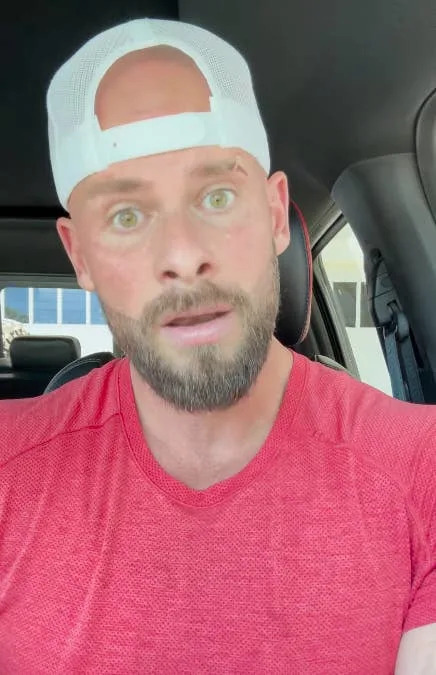 Man in a casual cap and t-shirt sits in a vehicle, looking directly at the camera