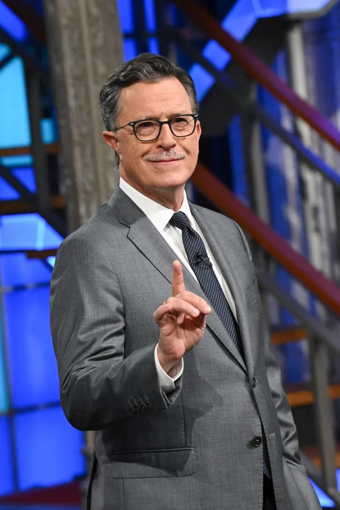 Man in a suit gestures on a talk show set