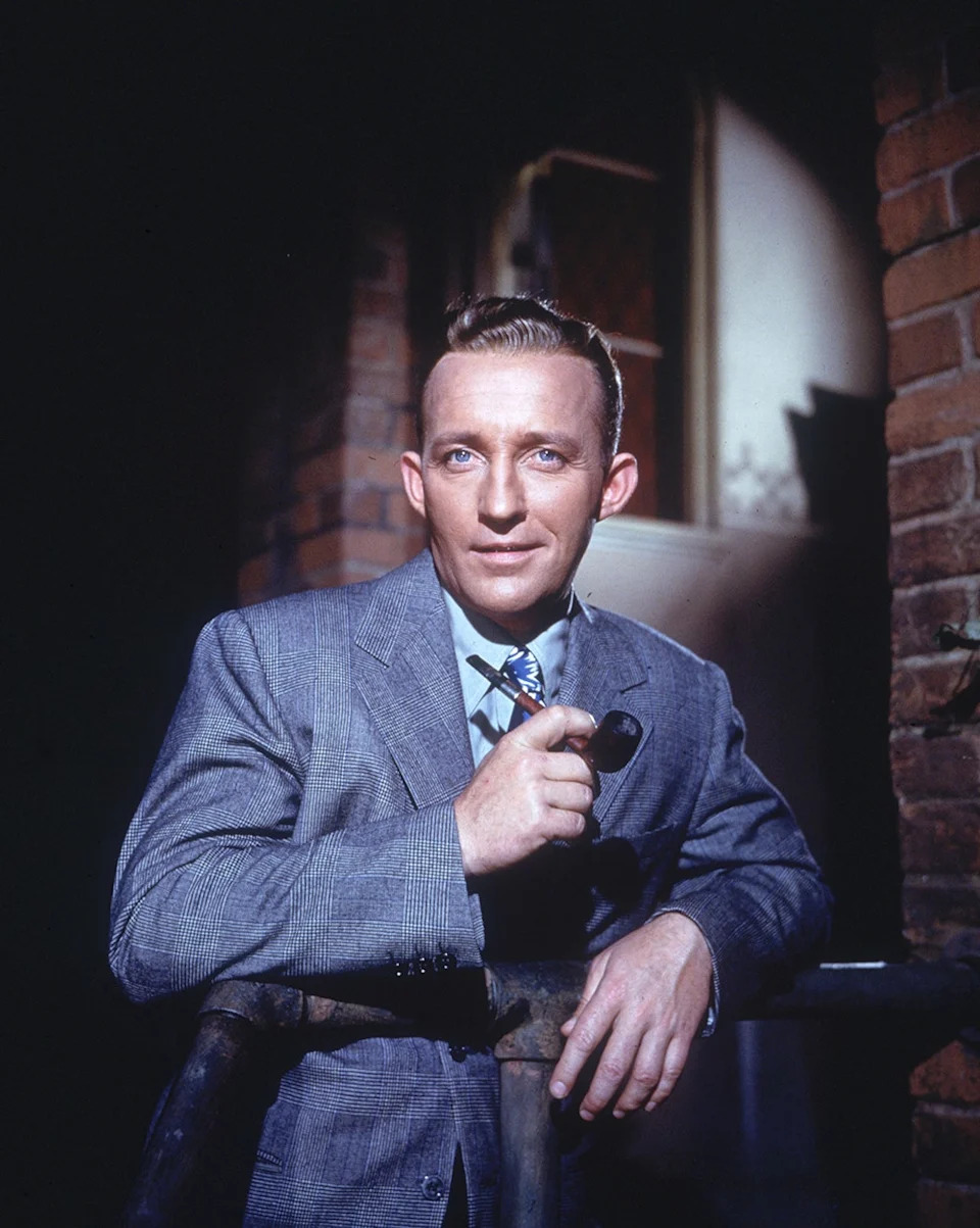 Bing Crosby in a blue suit posing with a smoking pipe.