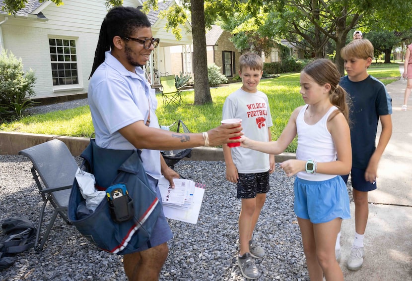 USPS mail carrier Khalil Jackson receives a lemonade from Everly Wallace, 10, who is running...