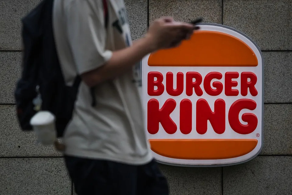 Person using phone walks past a Burger King sign attached to a wall