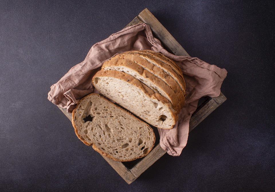 Sliced â€‹â€‹whole grain bread loaf lies on pink napkin in wooden box