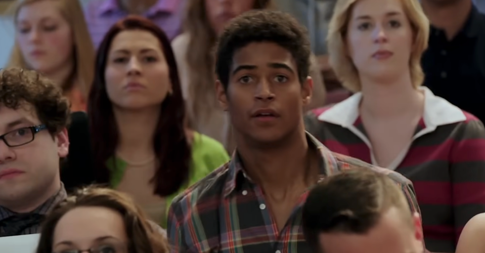 A group of people are seated, looking forward attentively, with a young man in a plaid shirt in focus