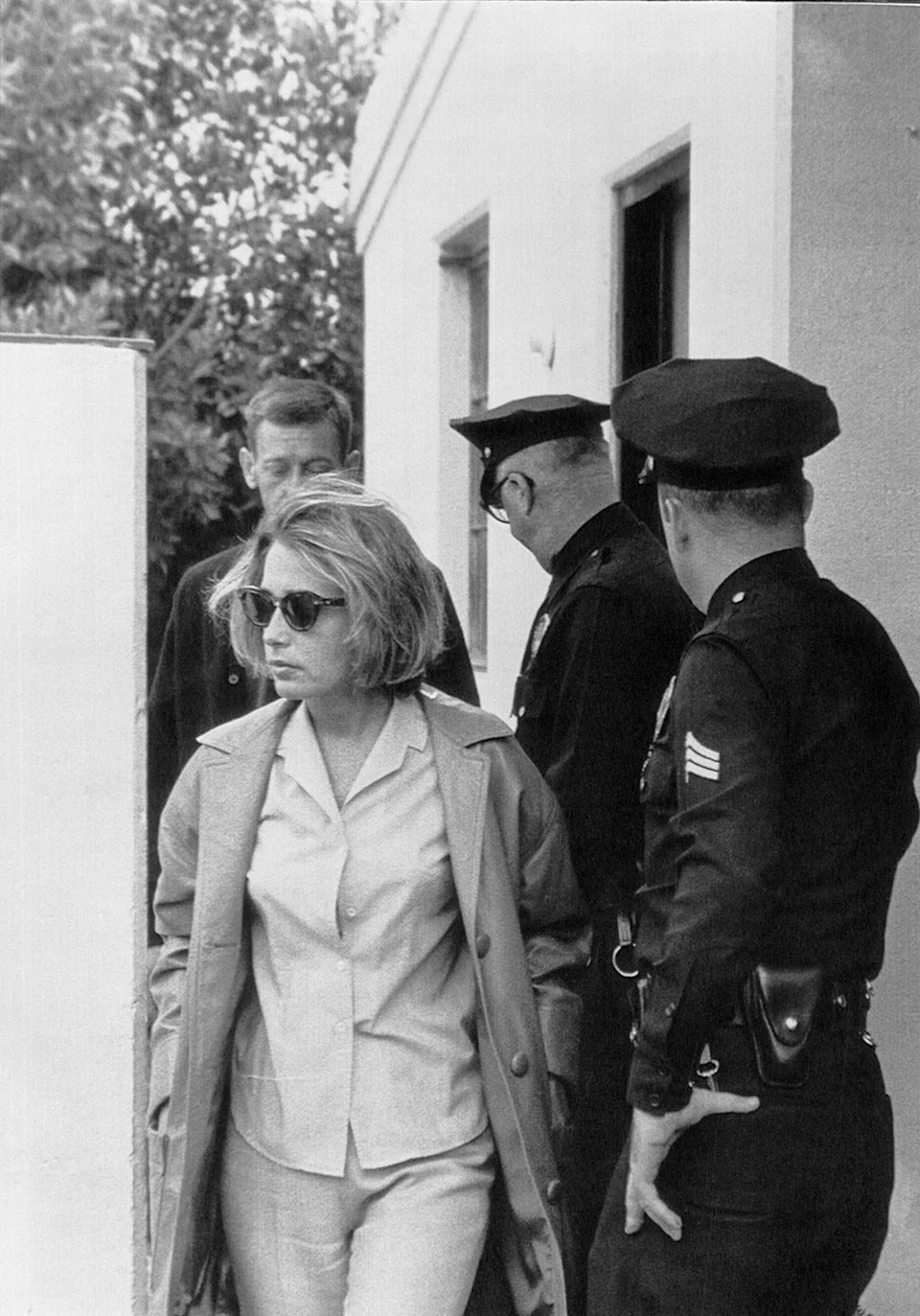 Pat Newcomb wearing sunglasses next to police.