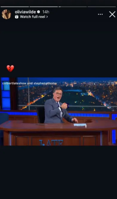 Late-night host in suit gestures at desk during show. Image tagged with 'colbertlateshow' and 'stephenathome'. Red broken heart emoji added
