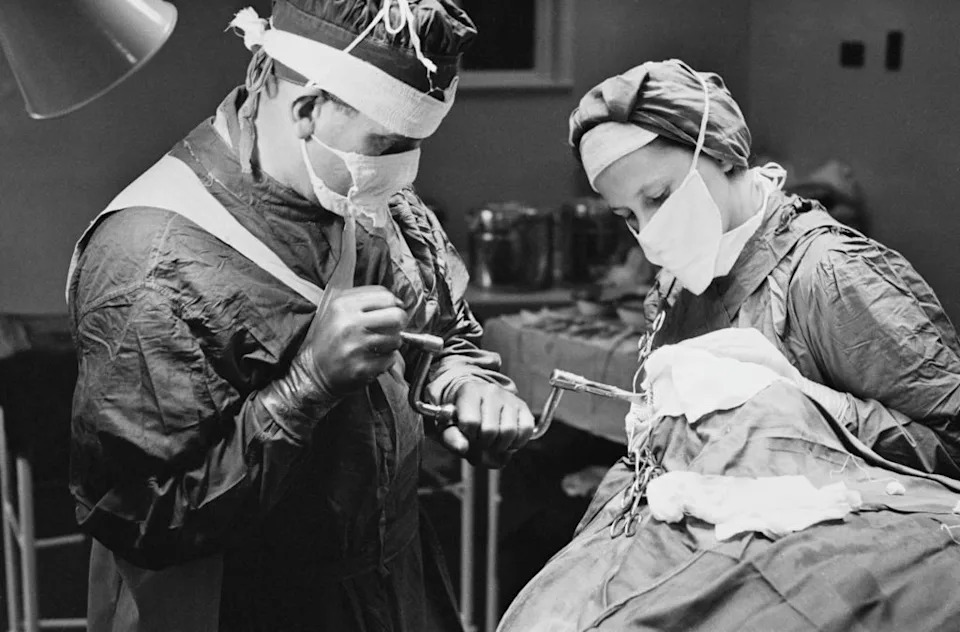 Surgeons in protective clothing perform a procedure on a patient using medical tools in an operating room