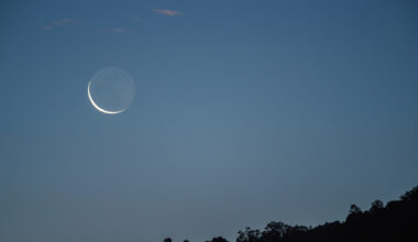 A waning crescent moon is pictured rising in the morning sky above a dark horizon.