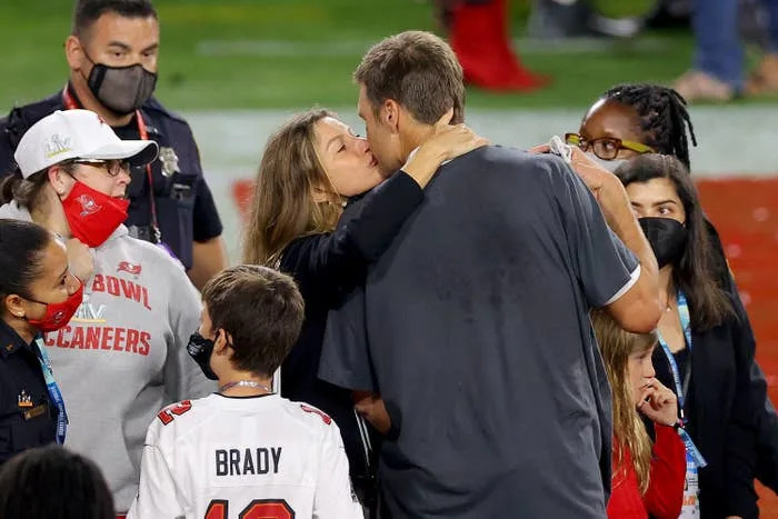 A person in a sports jersey is surrounded by family and fans, being embraced by someone amid a crowd, likely post-event celebration
