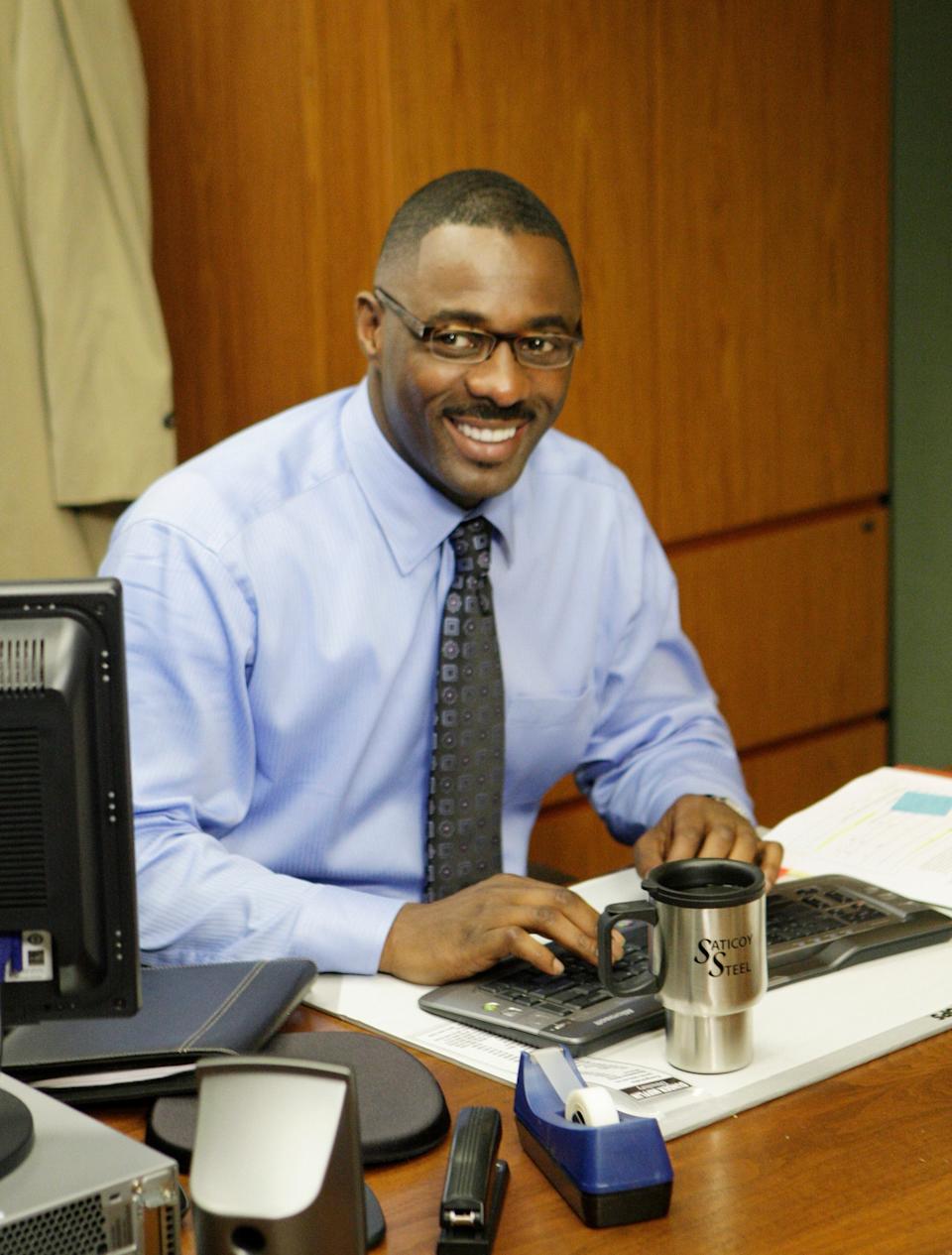 Man smiling while sitting at a desk with a keyboard and a "Scranton Strangler" coffee mug. He's wearing a light dress shirt and tie
