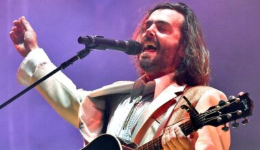 Lord Huron singer Ben Schneider on stage in a white suit with mouth open and eyes closed mid song, with one hand on a guitar neck and the other in the air. At the 2022 Bonnaroo Music & Arts festival in Tennessee.