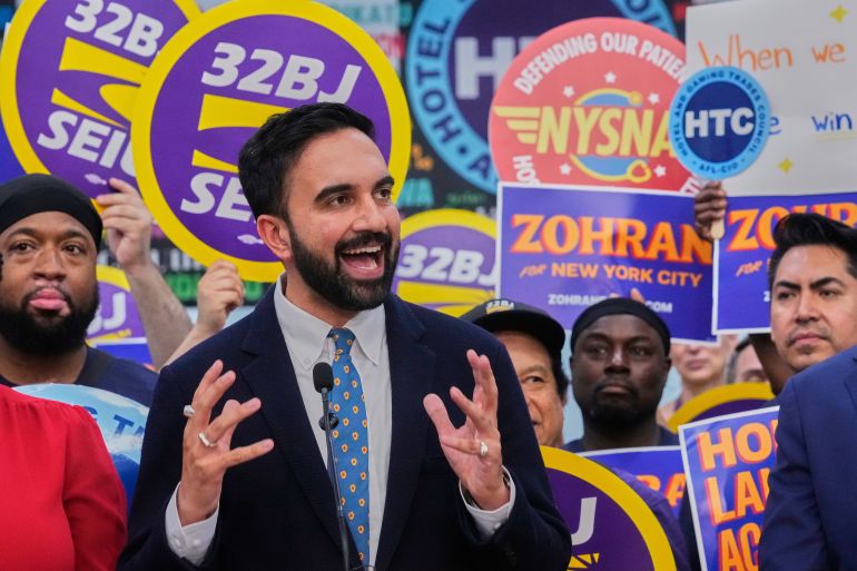 Zohran Mamdani at a rally, surrounded by supporters waving signs