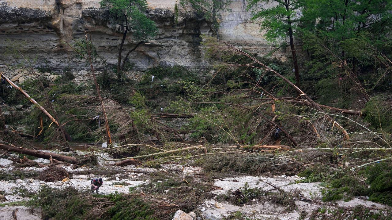 A Texas Department of Public Safety official, bottom left, combs through the banks of the Guadalupe River near Camp Mystic after a flash flood swept through the area Saturday, July 5, 2025, in Hunt, Texas. (AP Photo/Julio Cortez)