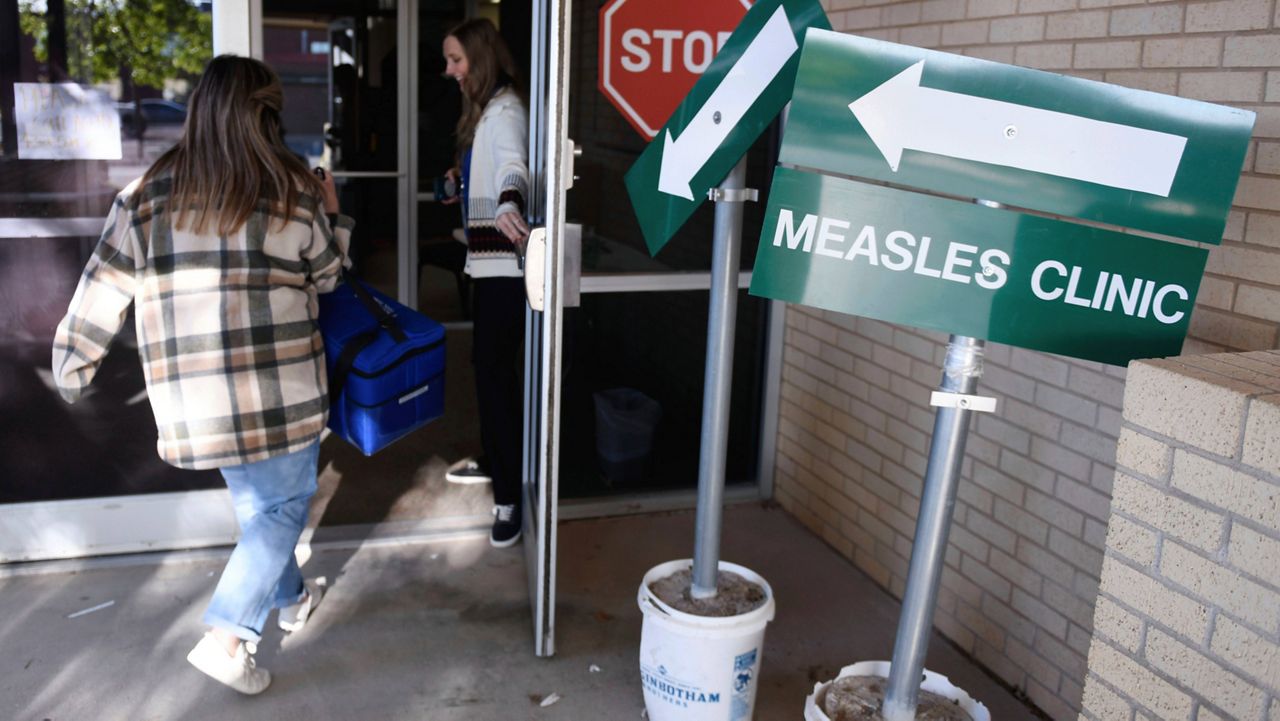 Health department staff members enter the Andrews County Health Department measles clinic carrying doses of the measles, mumps and rubella vaccine, Tuesday, April 8, 2025, in Andrews, Texas. (AP Photo/Annie Rice)