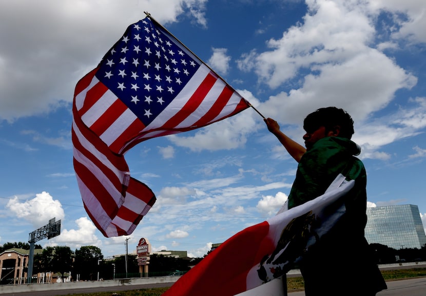 An attendee waves an American flag as motorists honk while passing during an ICE vigil held...