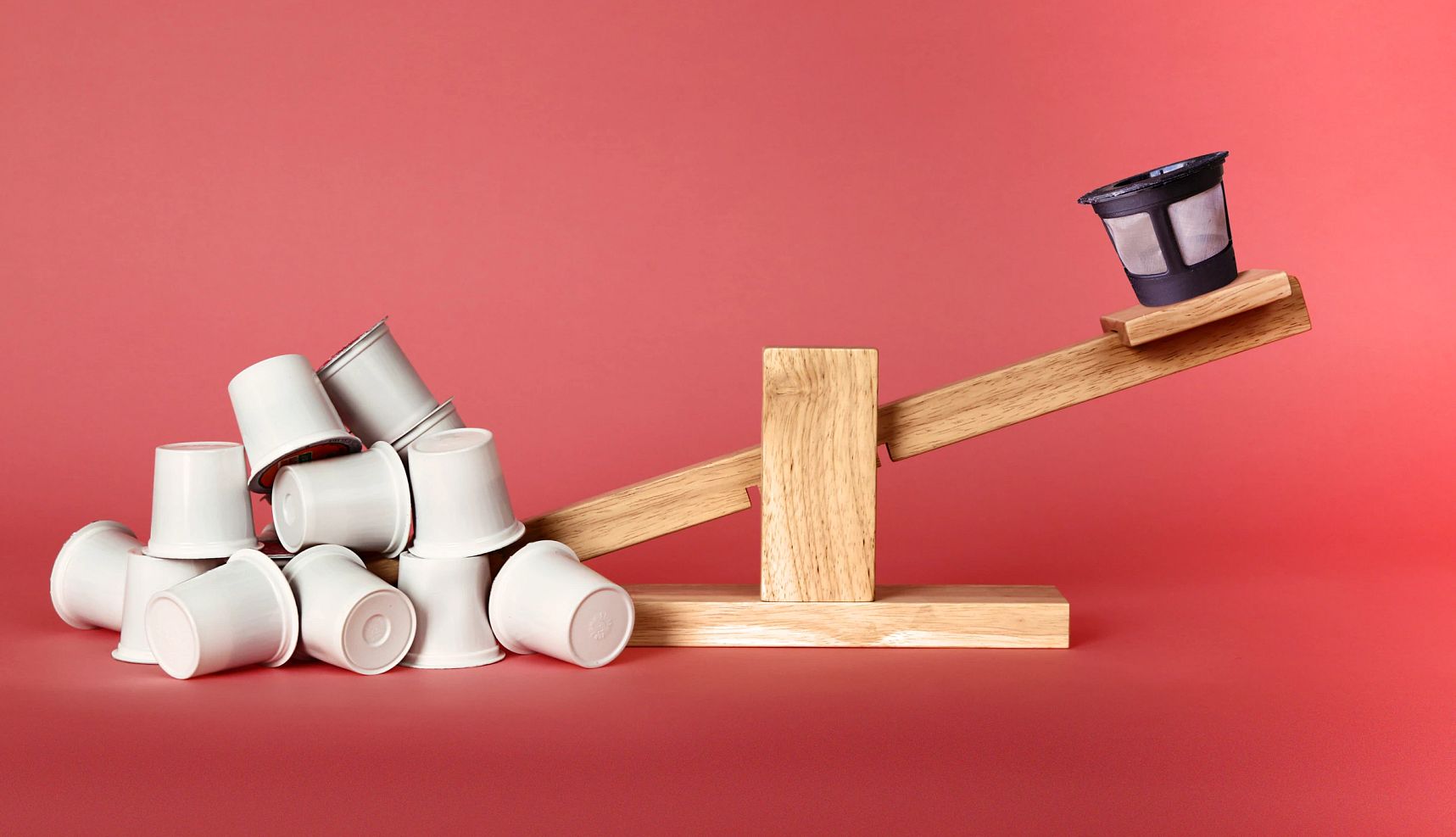 a seesaw with single use coffee pods on one end and a reusable coffee pod on the other