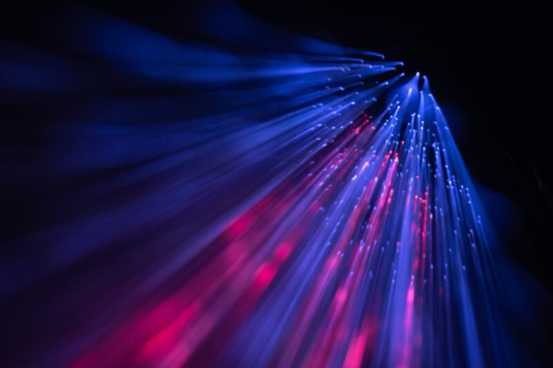 Streaks of blue and pink light extend diagonally across a dark background, creating an abstract, glowing, fiber-optic effect.