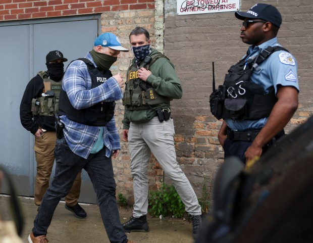 Masked federal agents walk past a Chicago police officer standing in the alley behind the Intensive Supervision Appearance Program office, ISAP, run by Immigration and Customs Enforcement, in the South Loop on June 4, 2025. (Eileen T. Meslar/Chicago Tribune)