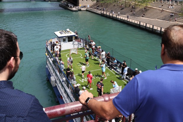 People along the LaSalle Street bridge look on as New York Charging (in blue) play against the Maryland Charm (in red) in a first-ever-lacrosse game on a boat on the Chicago River on July 10, 2025. (Antonio Perez/Chicago Tribune)