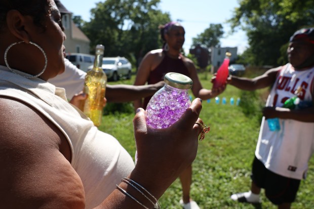 Alisha Black, center-back, hands out glass bottles filled with scented colorful beads to residents attending the unBlocked Englewood block party in the 6500 block of South Aberdeen Street on June 28, 2025. Black uses the beads for chromotherapy and aromatherapy for adults and children. (Chris Sweda/Chicago Tribune)