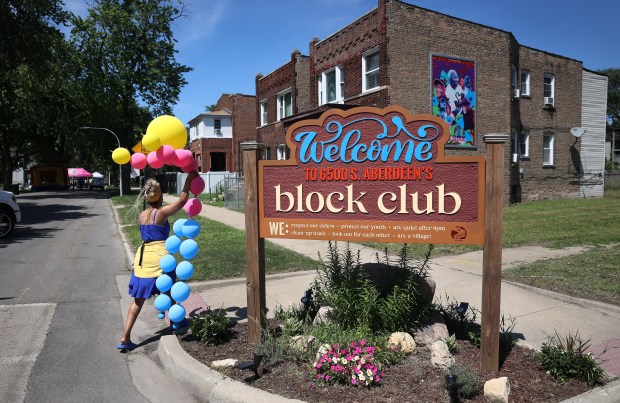 Janell Nelson carries balloons past a new 6500 S. Aberdeen block club sign during the unBlocked Englewood block party on June 28, 2025. (Chris Sweda/Chicago Tribune)
