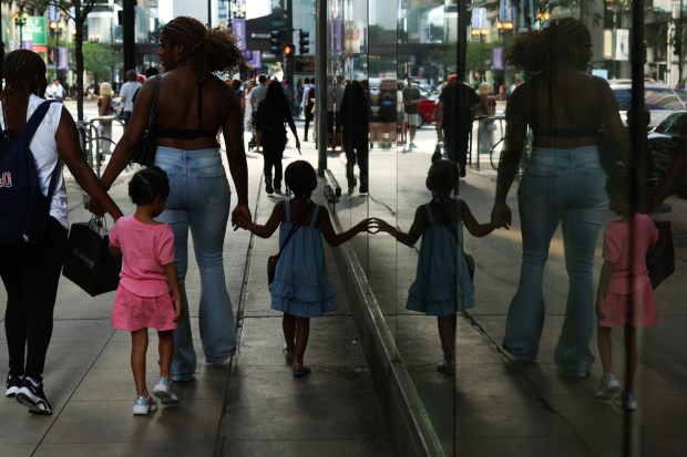 A child touches a storefront window while walking with her...