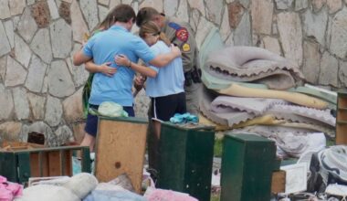 An officer prays with a family as they pick up items at Camp Mystic in Hunt, Texas on Wednesday, July 9, 2025. (AP Photo/Ashley Landis)