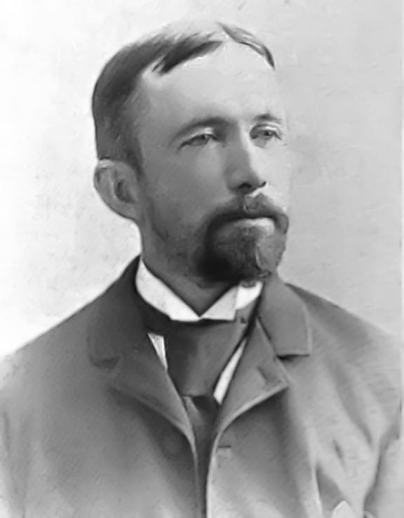 Black and white portrait of a man with short hair, a mustache, and a beard, wearing a suit and tie, facing slightly to the right.