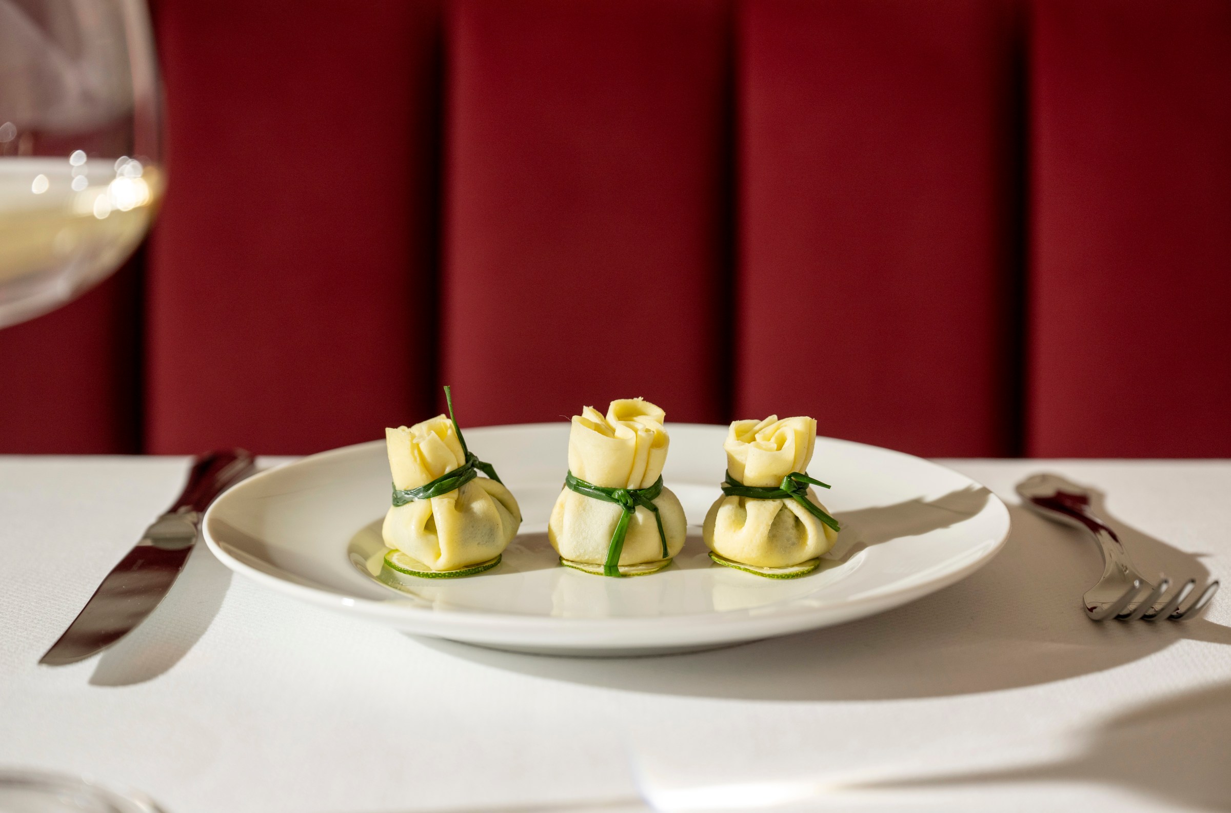 Three dumplings on a plate with green ties.