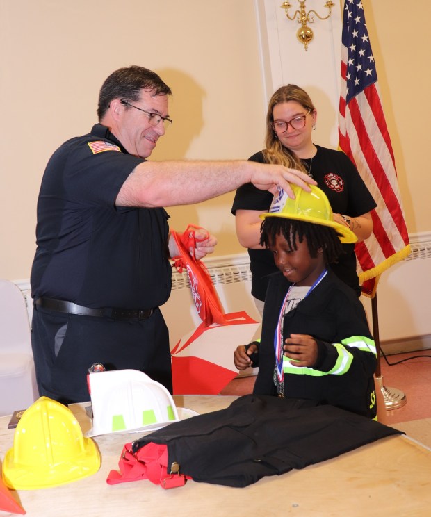 Collingdale Fire Company's fire prevention officers Steve Zane and MacKenzie Hays present Kah'ir Gibson with his own fireman's jacket. emblazoned with his name and the fire company's name, as well as a fire hat, bobblehead, and a medal and plaque acknowledging the young boy's brave actions. (COURTESY OF JOY WINNER)