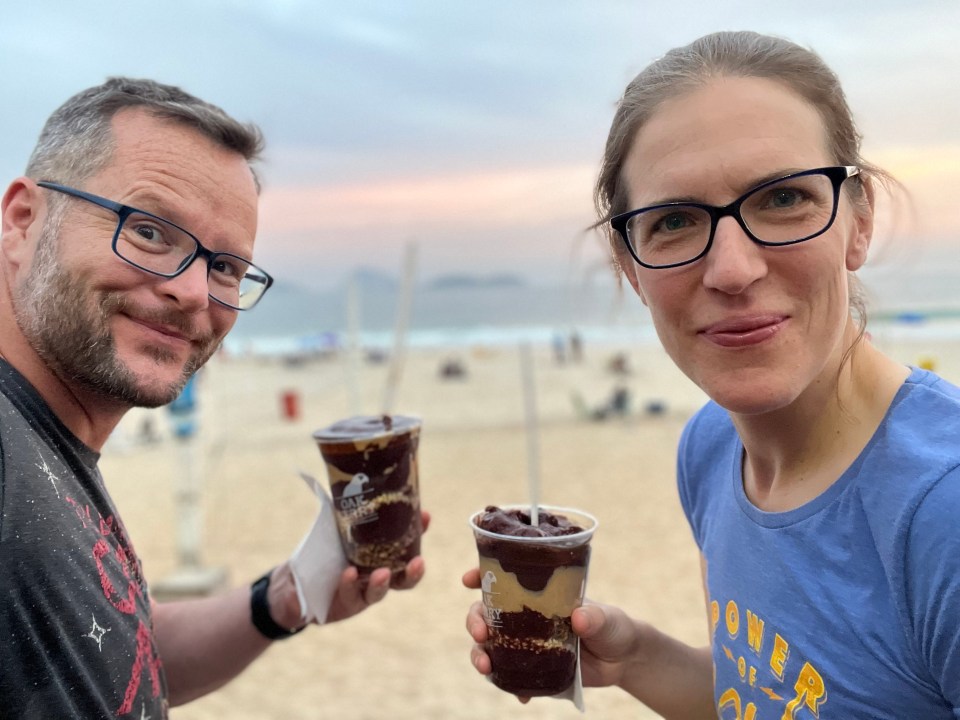 Couple on a beach holding acai bowls.