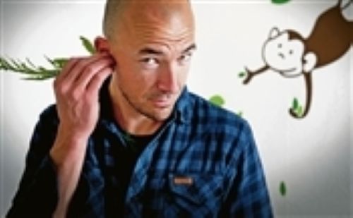 A bald man sticking some leaves in his ear  with a drawing of a money behind him.