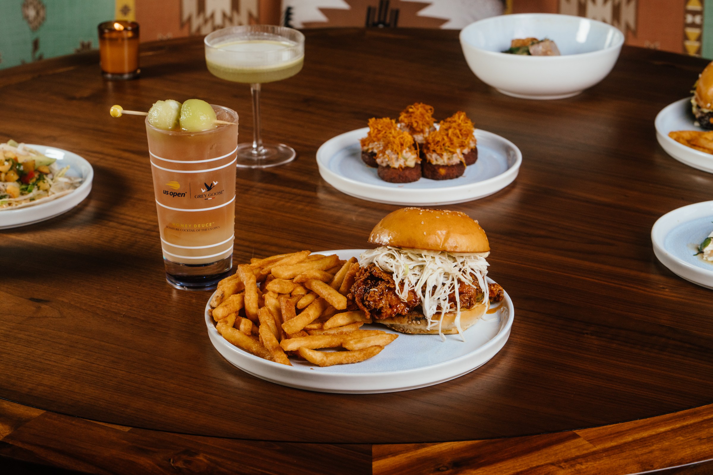 A fried chicken sandwich sits on a plate with fries and a glass of beer behind.
