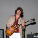 A man holding a guitar before an amp.