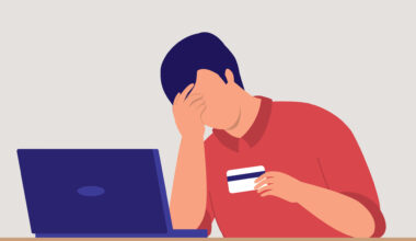 A vector illustration of someone with one hand to their face and a credit card in the other hand. They are sitting in front of a laptop on a table.
