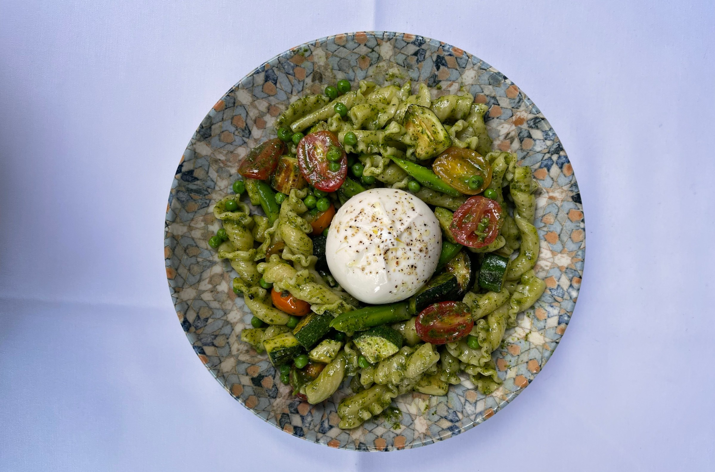 A bowl of pesto-covered noodles with burrata in the middle.