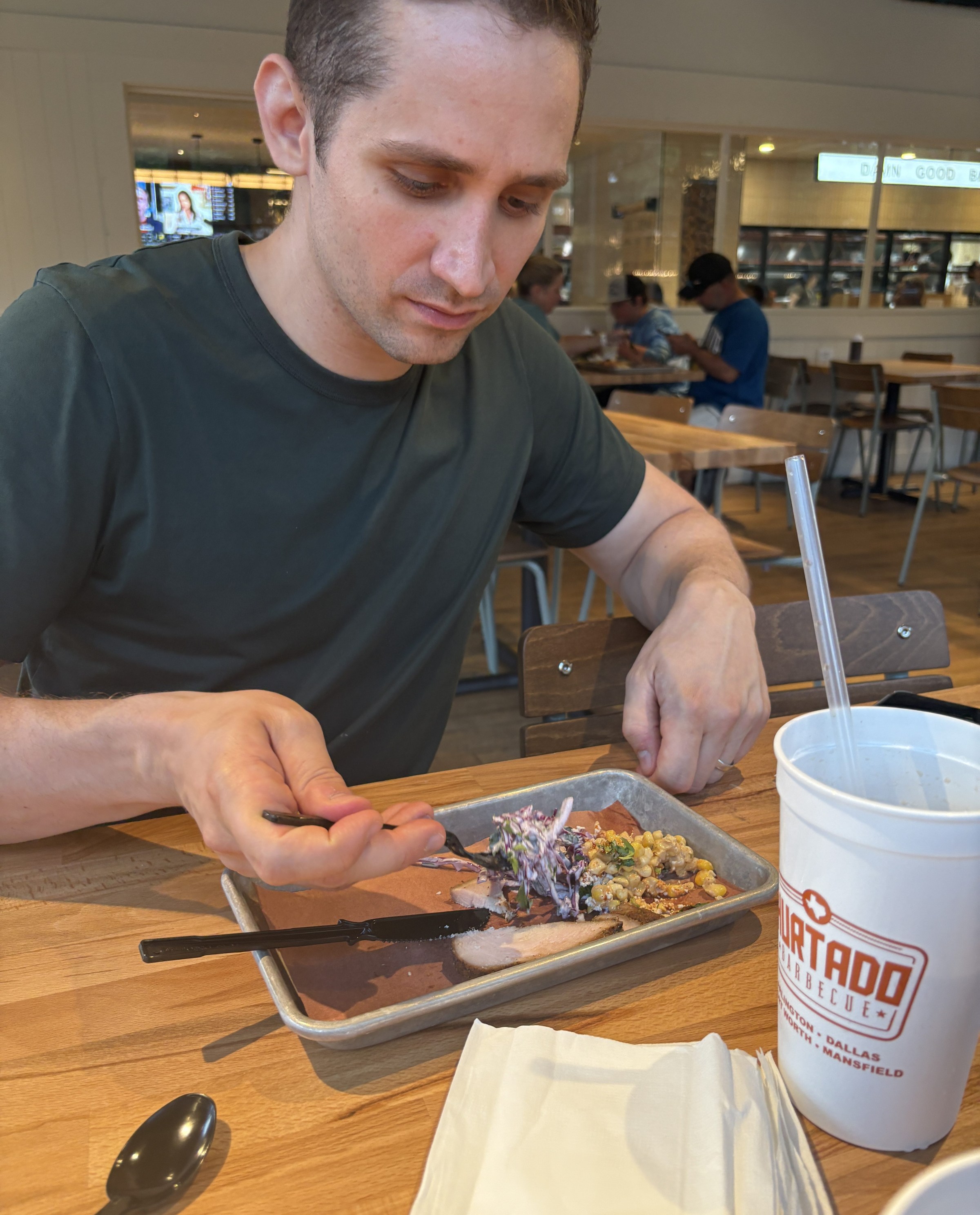 A man sits at a table, eating barbecue from a tray.